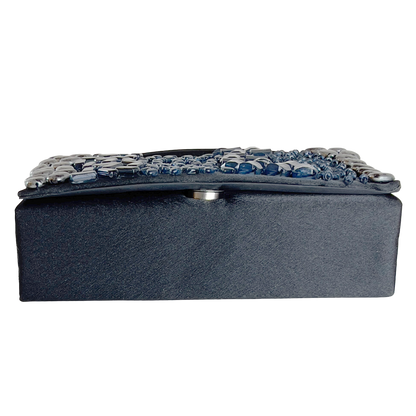 Black clutch with decorative blue stones laying flat, showing the bottom, on a white background