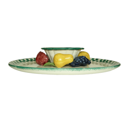 Ceramic plate with decorative edge holding small ceramic fruits on a white background