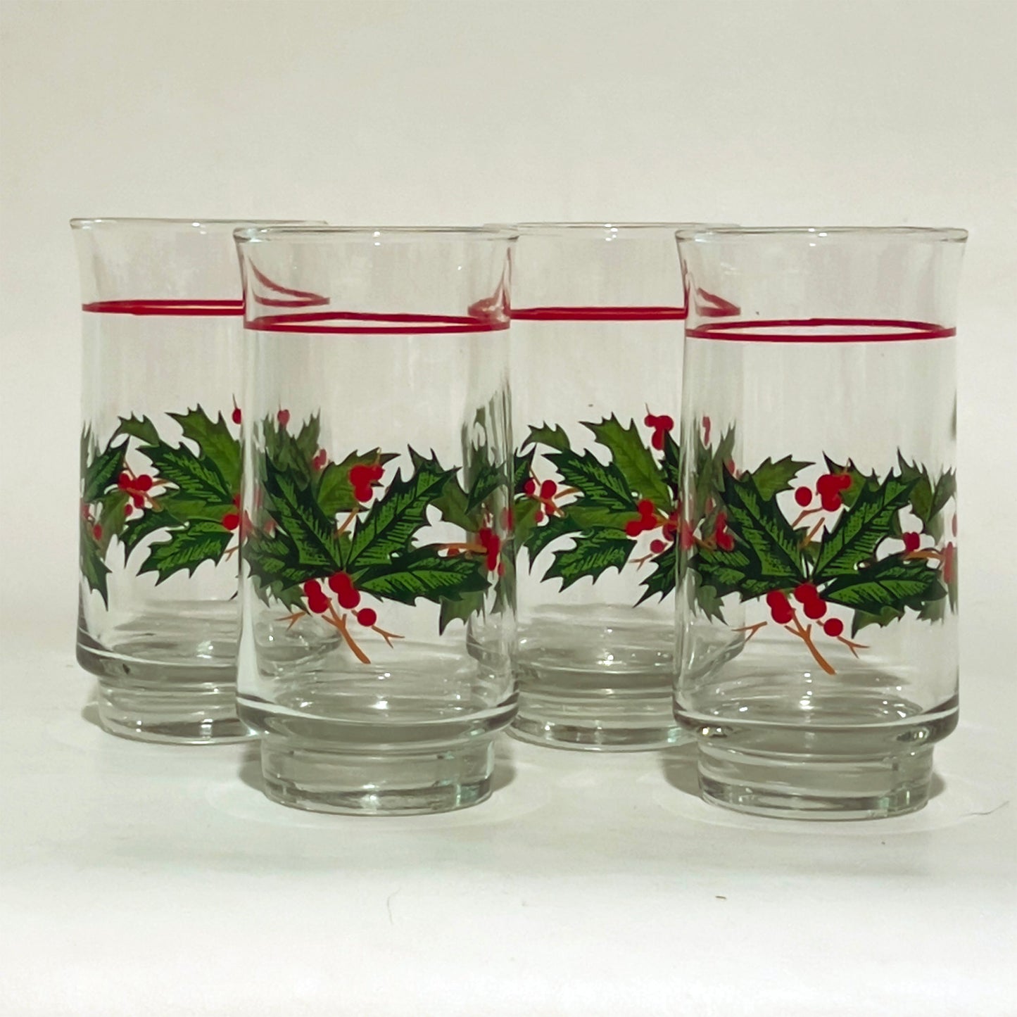 Set of four glass tumblers with holly design on a white background