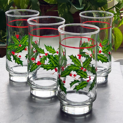 Four glass tumblers with holly design on a reflective surface.