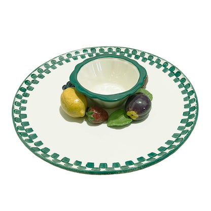 Ceramic plate with green rim and decorative edge, featuring a small bowl and fruit-shaped objects on a white background.