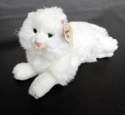 A white Angora plush cat toy with blue eyes, made of laying on a black surface.