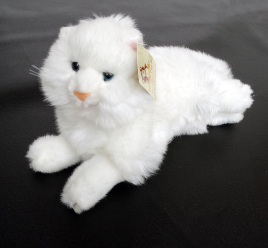 A white Angora plush cat toy with blue eyes, made of laying on a black surface.